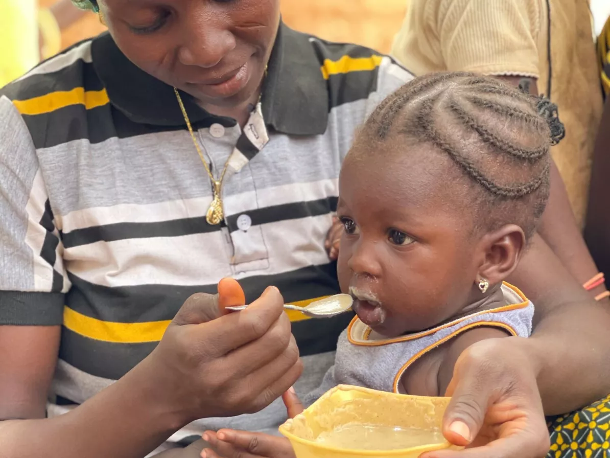 A woman feeds a baby from a yellow bowl